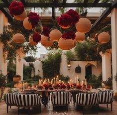 an outdoor dining area with black and white striped chairs, red flowers hanging from the ceiling