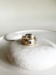 two gold wedding rings sitting on top of a white rock in the middle of a room