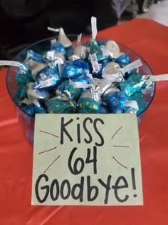 a glass bowl filled with blue and silver candies next to a sign that says kiss go goodbye