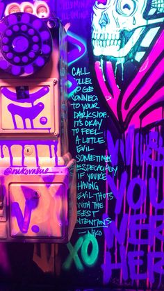 the wall is covered in graffiti and has two telephones attached to it with neon colors