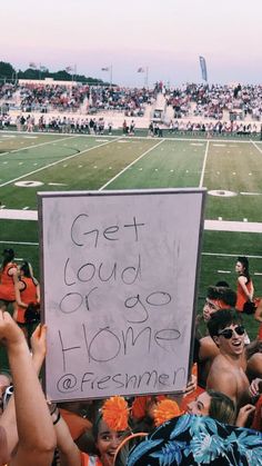 a group of people sitting on top of a football field holding up signs that read get loud or go home