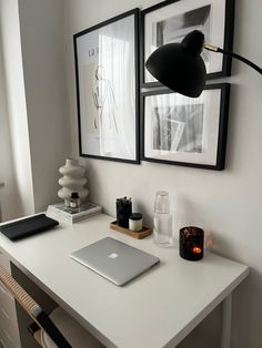 a laptop computer sitting on top of a white desk next to two black framed pictures