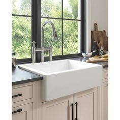 a white kitchen sink sitting under a window next to a wooden cutting board and utensils