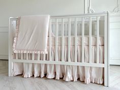 a white crib with pink ruffled bedding and pillows on the bottom rail