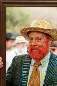 a man with a red beard wearing a straw hat and colorful suit is reflected in a mirror