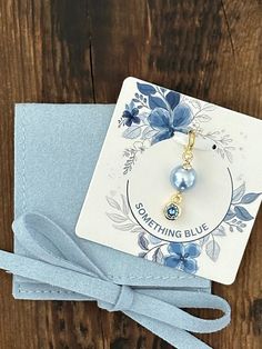 a card with a blue ribbon tied around it on top of a wooden table next to a tag that says something blue