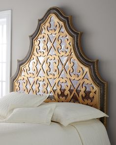 a bed with white linens and gold headboard next to a window in a bedroom