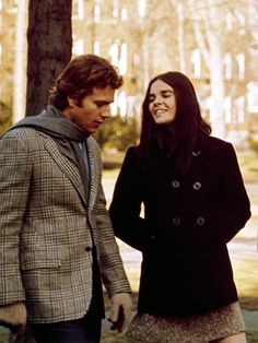 a man and woman standing next to each other in front of a tree with leaves on it