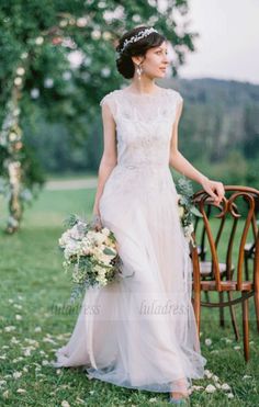 a woman standing next to a wooden chair holding a bouquet in her hand and wearing a wedding dress