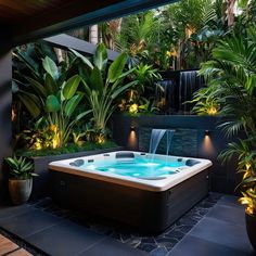 an outdoor hot tub surrounded by plants and water features lights on the sides, along with potted greenery