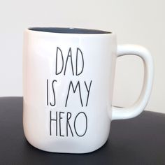 a white coffee mug with the words dad is my hero on it sitting on a table