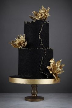 a black and gold wedding cake with flowers on top