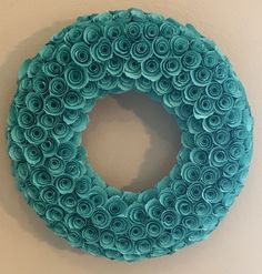 a wreath made out of rolled up blue paper flowers on a wall with a white background