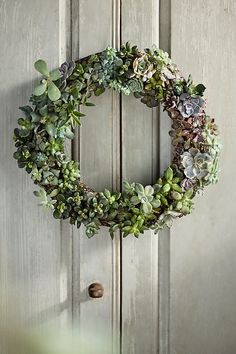 a wreath hanging on the front door of a house with succulents in it