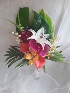 a bouquet of flowers sitting on top of a white cloth covered table next to green leaves