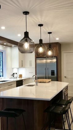 a kitchen with three lights hanging from the ceiling and two bar stools in front of it