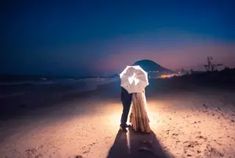 a man and woman are standing on the beach at night under an umbrella with their arms around each other