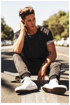 a man sitting on top of a skateboard next to a street with trees in the background