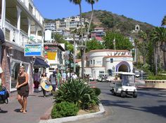 people are walking down the street in front of buildings and palm trees on a sunny day