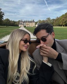 a man and woman sitting next to each other in front of a car with a castle in the background