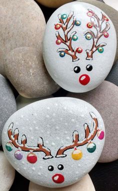 two painted rocks sitting on top of each other next to some rocks with reindeer's faces