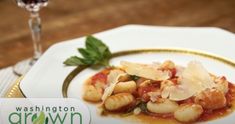 a white plate topped with pasta and garnish next to a glass of wine