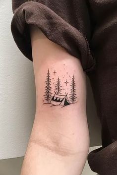 a person with a small tattoo on their arm that has trees and a tent in the background