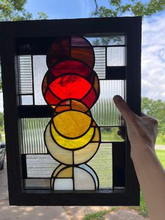 a hand holding up a stained glass window in front of a tree and grass area