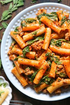 pasta with meat and spinach in a white bowl on a wooden table next to utensils