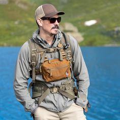 a man standing in front of a body of water wearing a brown hat and backpack