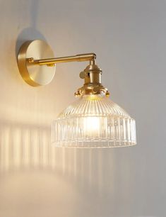 a light that is on the side of a white wall with a glass shade hanging from it