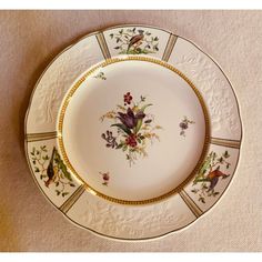 a plate with flowers and birds painted on the side, sitting on a tablecloth