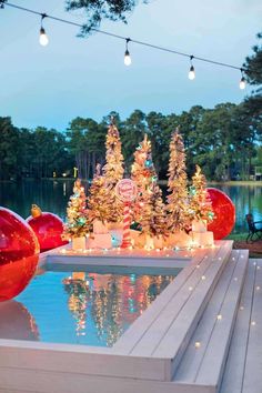 an outdoor christmas scene with lighted trees and ornaments on the water's edge at dusk