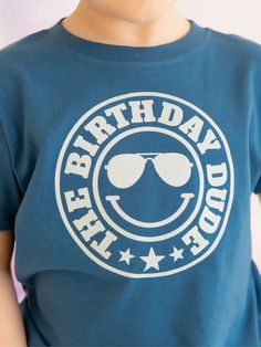 About this product The Birthday Dude Short Sleeve T-Shirt is a fun and festive t-shirt for celebrating the birthday boy! Features: Shirt Color: Indigo Graphic Color: White Material: 100% Cotton Features: Tagless inside neck label for an itch-free wear Fit: Toddler Unisex; True to Size Care: Machine washable, tumble dry low, wash with like colors Each t-shirt is hand pressed with love using baby and child safe inks. Details • Care Instructions: Machine wash • Fabric: 100% Cotton • Product Languag Fun T-shirt For Father's Day Birthday, Playful Birthday T-shirt With Text Print, Playful Text Print Birthday T-shirt, Playful Crew Neck T-shirt For Father's Day, Blue Cotton T-shirt For Birthday Gift, Fun Blue T-shirt For Father's Day, Playful Crew Neck T-shirt For Birthday Gift, Blue T-shirt For Father's Day Birthday, Blue T-shirt With Funny Print For Birthday