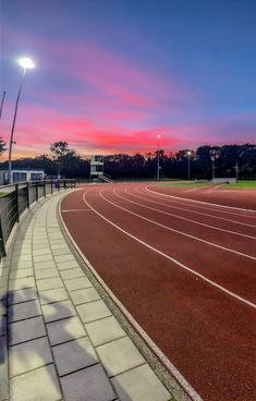 the sun is setting over an empty track in a stadium with red and white markings