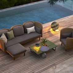 an outdoor living area with couches and tables next to a swimming pool at night