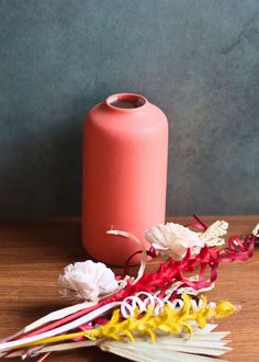 a pink vase sitting on top of a wooden table next to dried flowers and ribbons