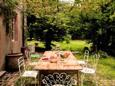 a wooden table with white chairs and plates on it in the middle of a yard