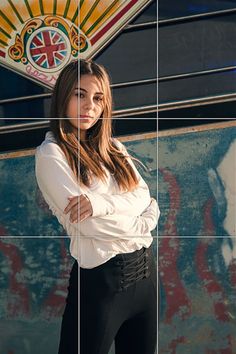 a woman standing in front of a wall with her arms crossed and looking at the camera