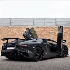 a black sports car parked in front of a brick wall with its doors open and the door opened