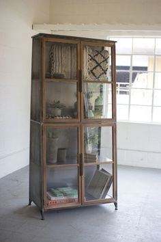 an old metal and glass cabinet with many items on it's shelves in front of a window