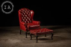 a red leather chair and footstool sitting in the middle of a dark room