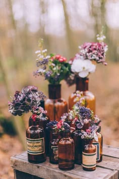 several bottles with flowers in them sitting on a wooden table outside by some bushes and trees