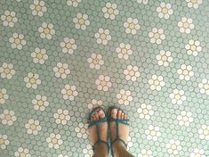 a person wearing blue sandals standing in front of a tiled wall with hexagonal tiles