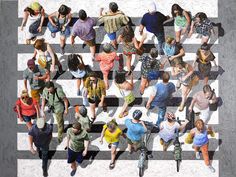 a group of people walking across a crosswalk in the middle of town, from above