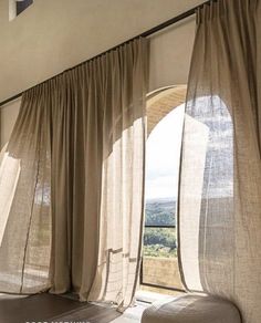 an open window with sheer curtains and a chair in the foreground, looking out onto a valley