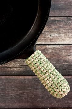 a green and white crocheted pot holder hanging from a black cast iron skillet