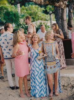 three women standing next to each other in front of a group of people on the beach