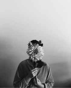 a black and white photo of a person holding a flower in front of their face