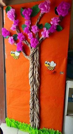 a paper plate tree with flowers on it and two bees hanging from the branches, in front of an orange wall